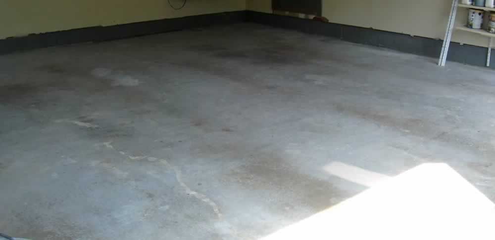 A concrete floor in a garage with a ladder in the corner.