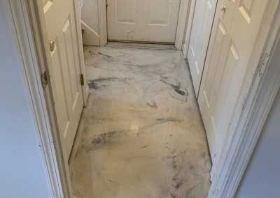 A hallway with a marble floor and white doors leading to a door.