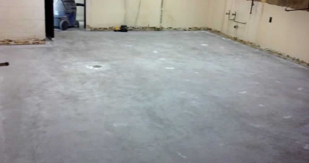 A dirty concrete floor in a room with a broom.