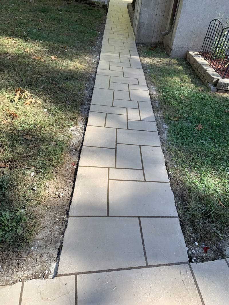A brick walkway leading to a house with grass on the side.