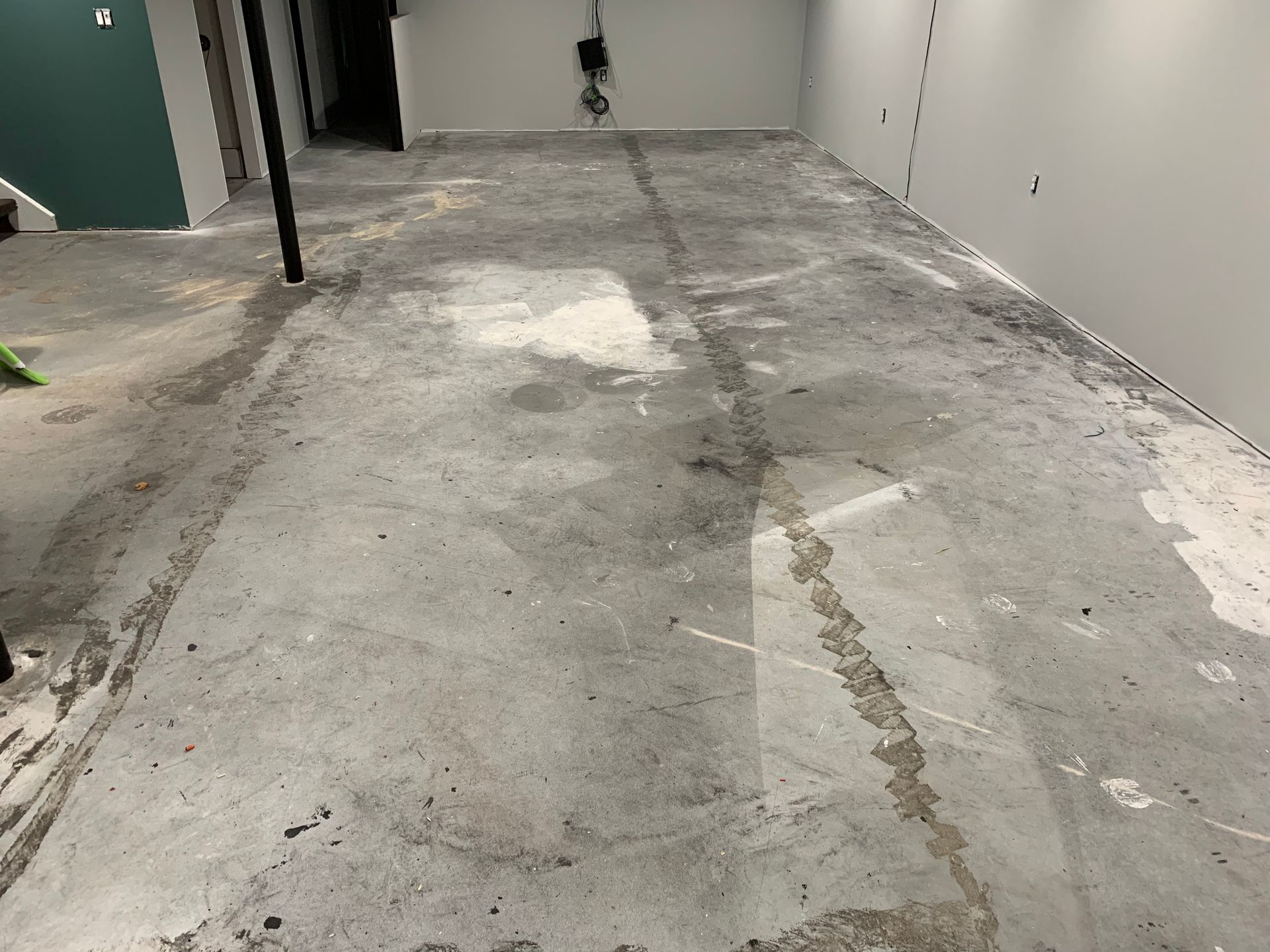 A concrete floor in a basement with a lot of stains on it.
