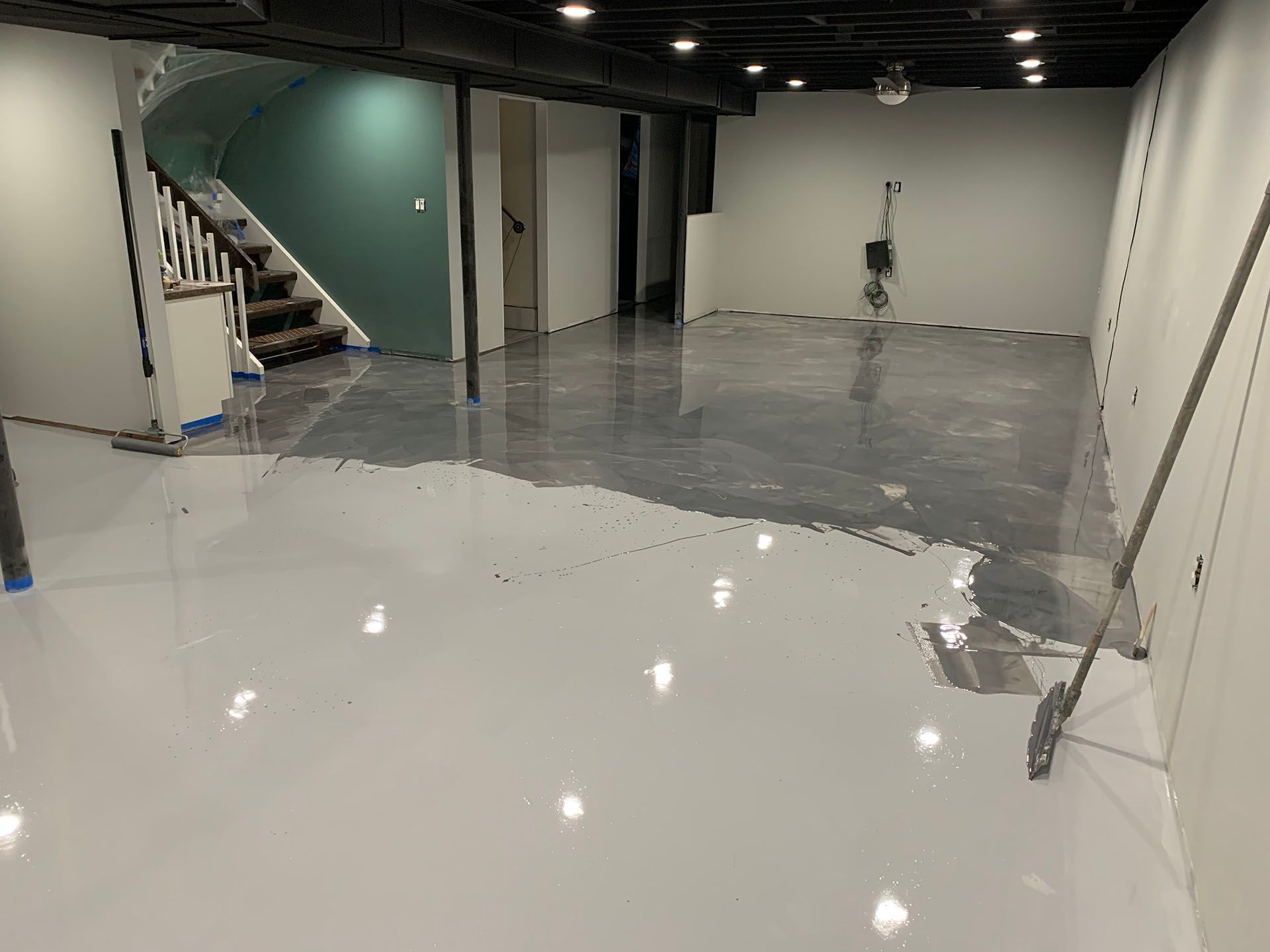 A basement is being painted white with a broom.