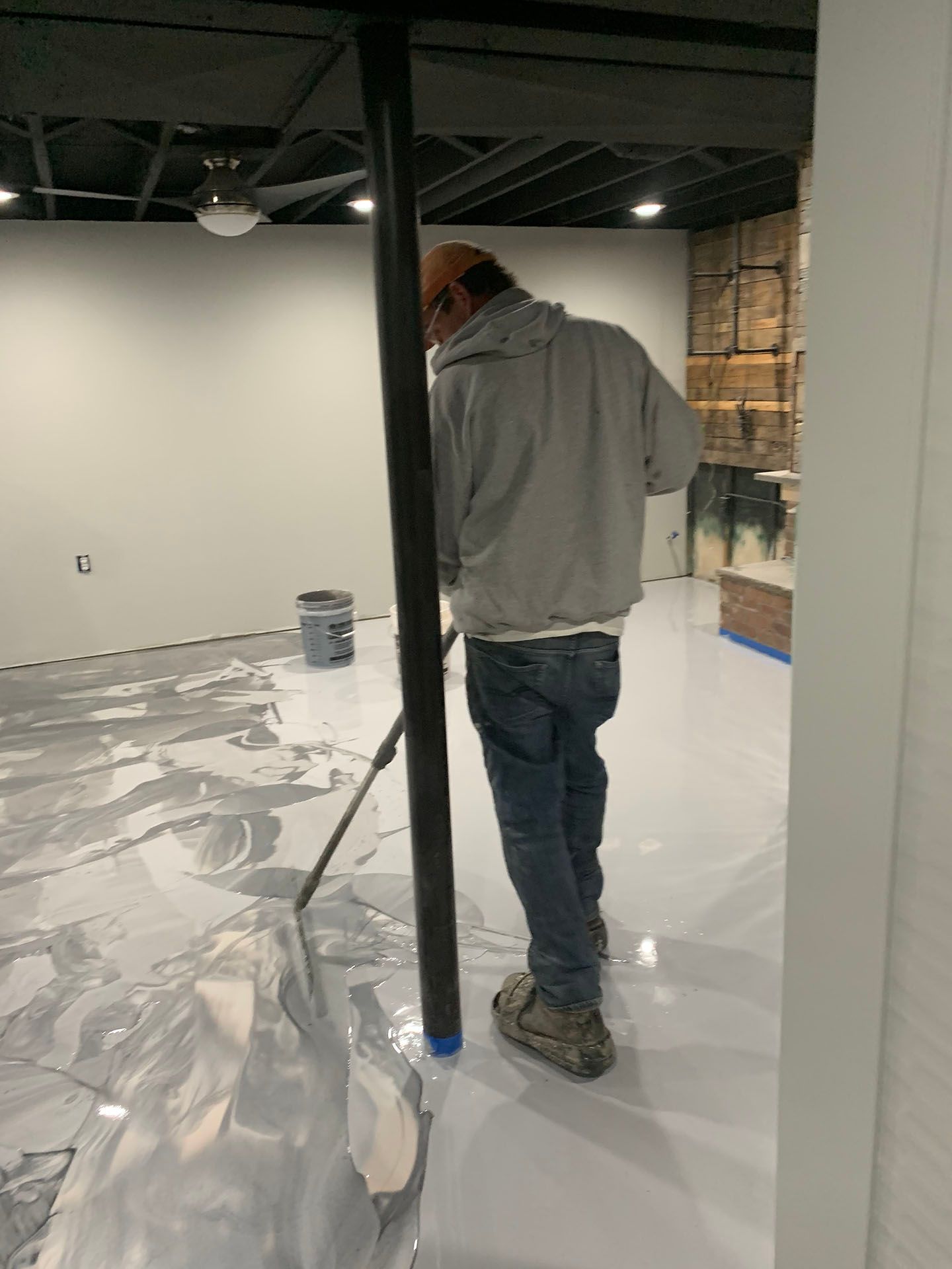A man is painting the floor of a room with a roller.