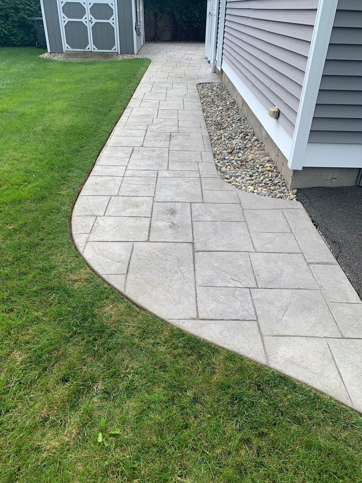 A sidewalk leading to a house with a shed in the background.