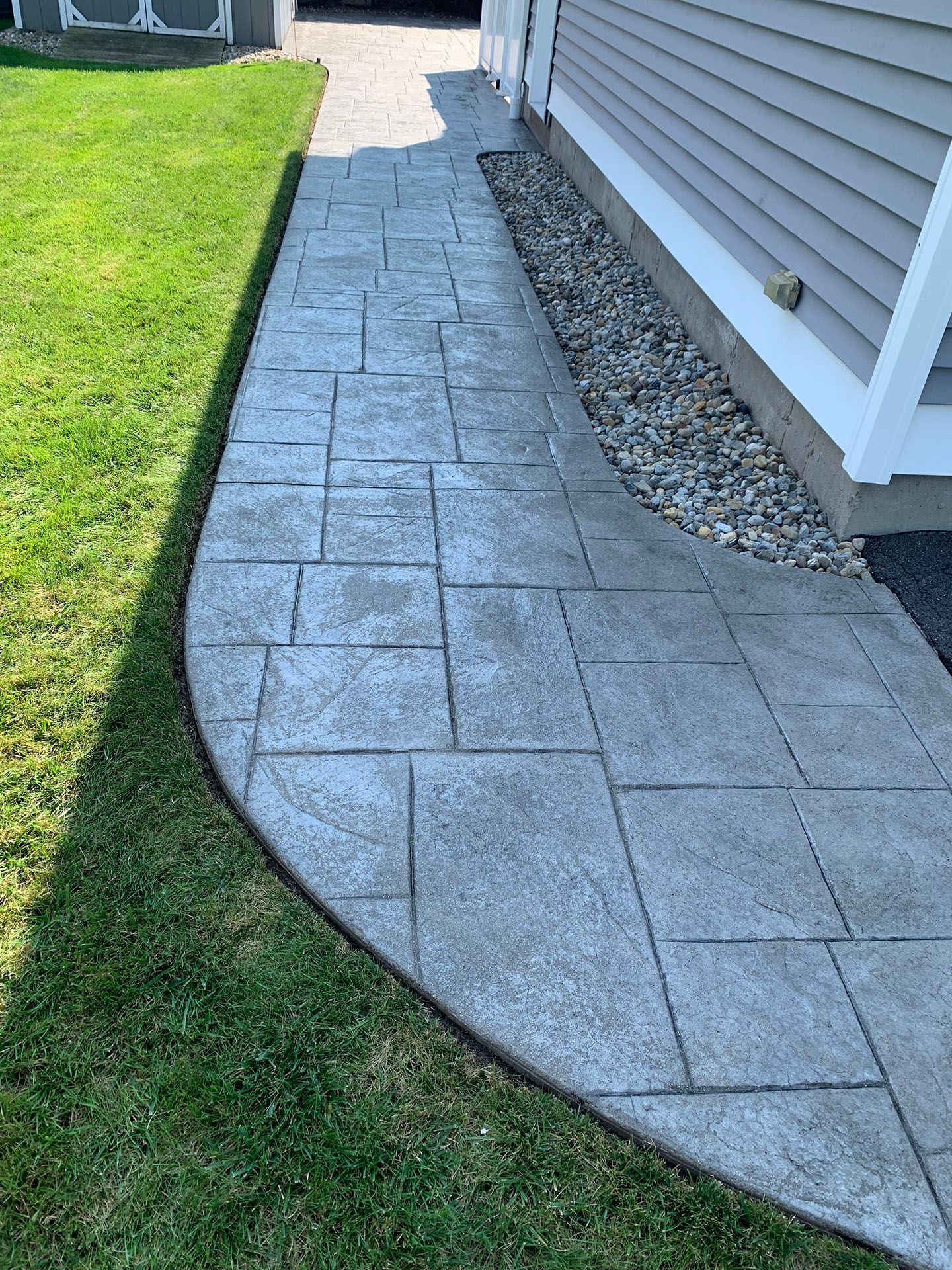 A concrete walkway leading to a house next to a lush green lawn.