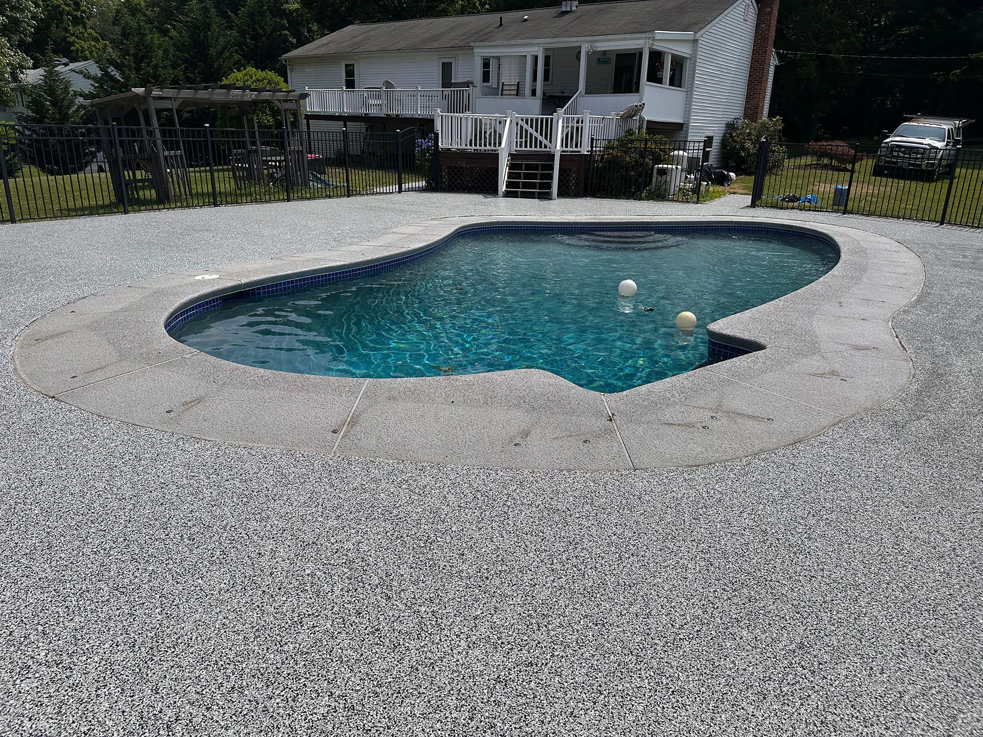 A large swimming pool is surrounded by gravel in front of a house.