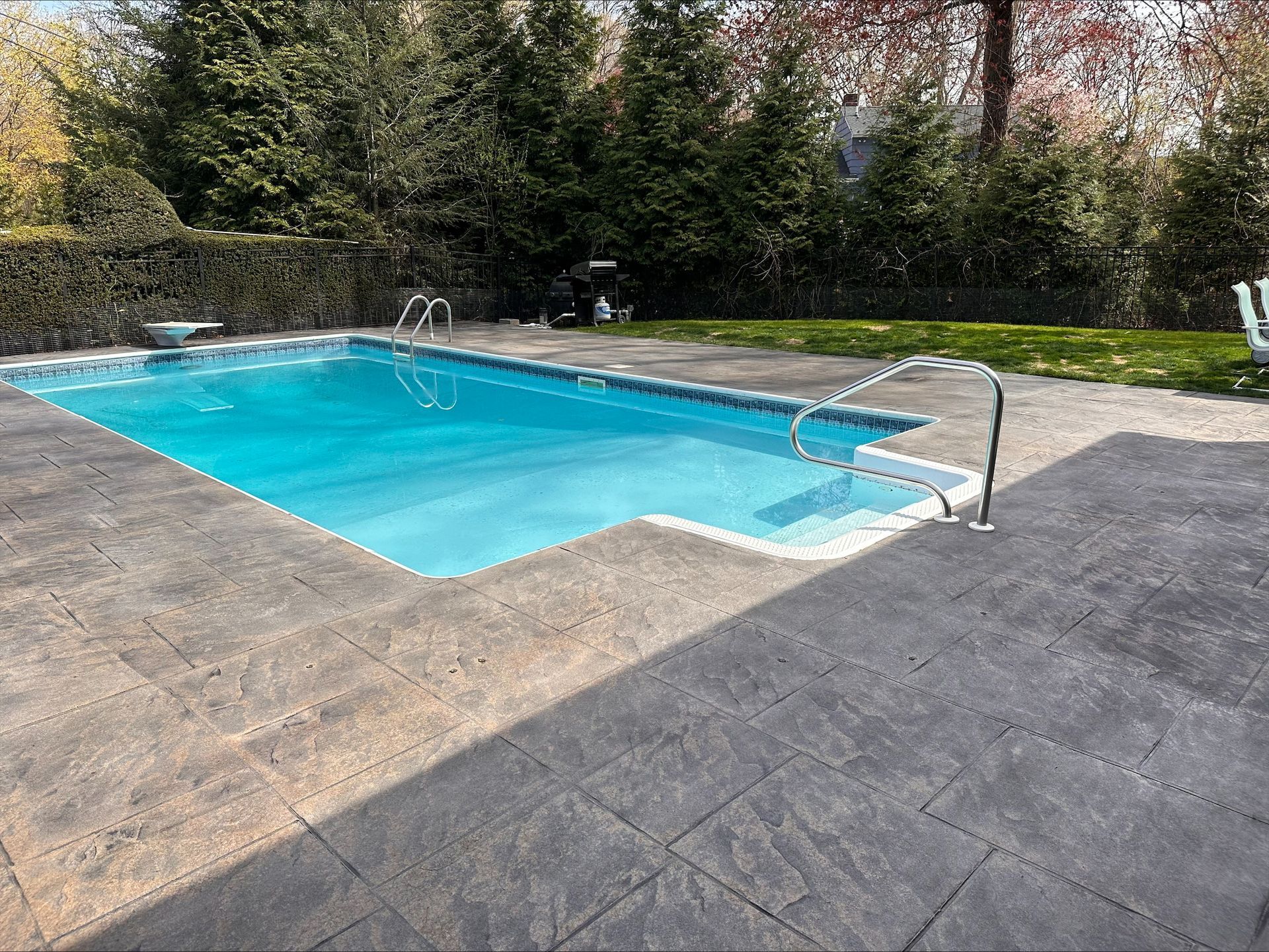 A large swimming pool is surrounded by trees and a patio.