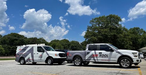 Two white utility trucks with logos parked side by side on a gravel lot under a blue sky