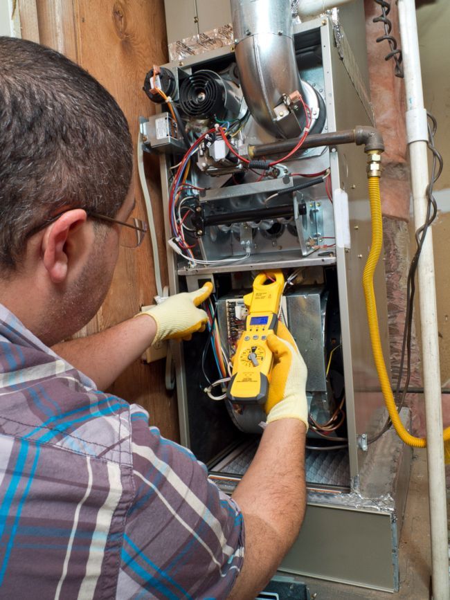 Technician using a yellow tool to service an open furnace in a utility closet