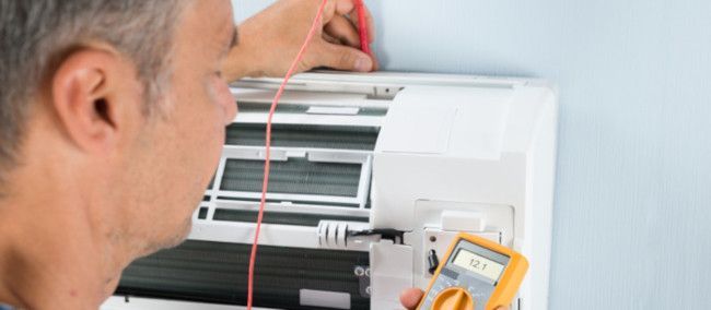 Person using a multimeter to inspect an air conditioner unit on a wall