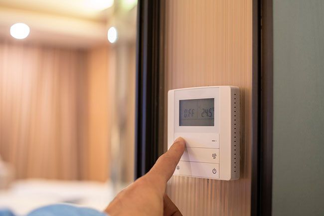 A hand pressing a wall-mounted thermostat in a softly lit room.