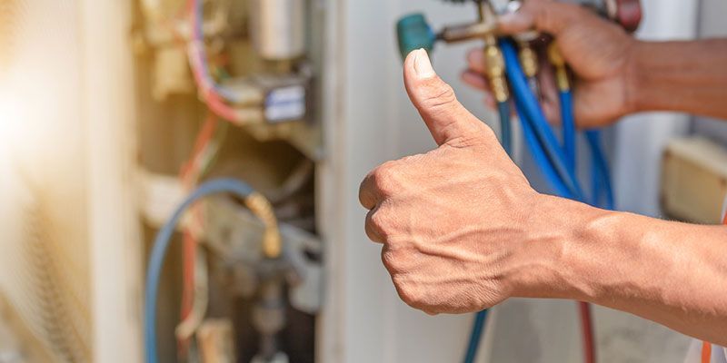 Hand giving a thumbs-up beside plumbing pipes and blue valves in a utility area