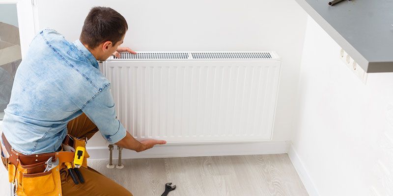 Worker installing a white radiator on a wall in a bright room