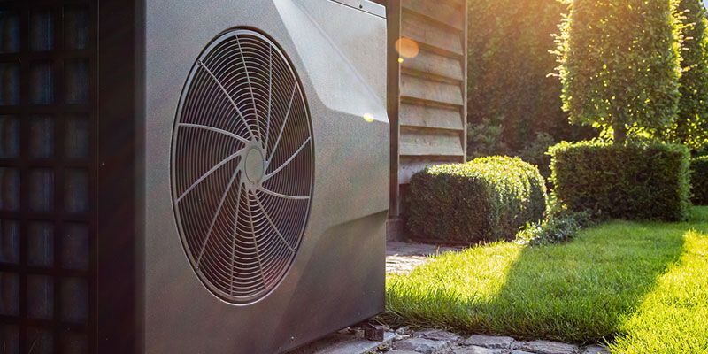 Outdoor HVAC unit beside a sunlit house, with a green lawn and shrubs in the background