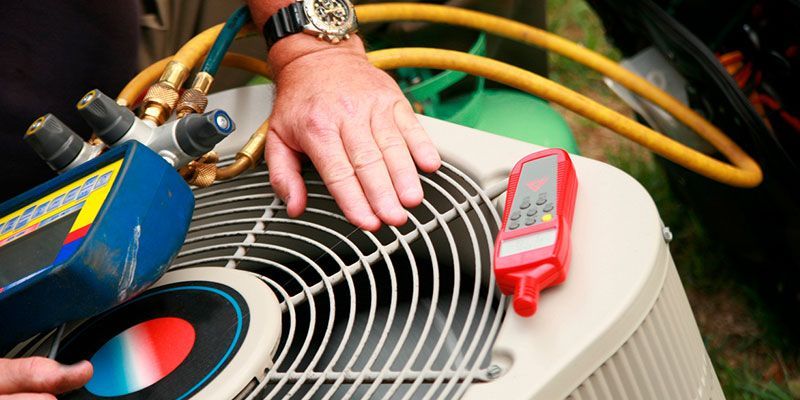 Technician’s hand on HVAC unit, with hoses and a red clamp meter on top