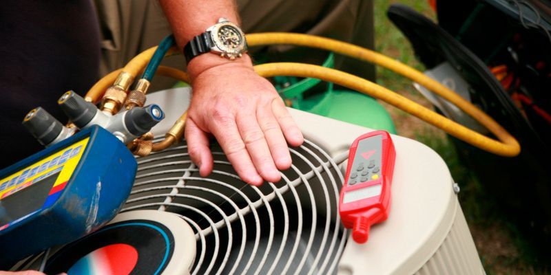 Technician’s hand on HVAC fan grille with hoses and a red gauge during maintenance