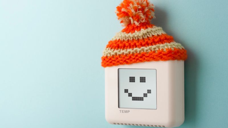 White smiling gadget wearing an orange knit winter hat with pom-pom on a light blue background