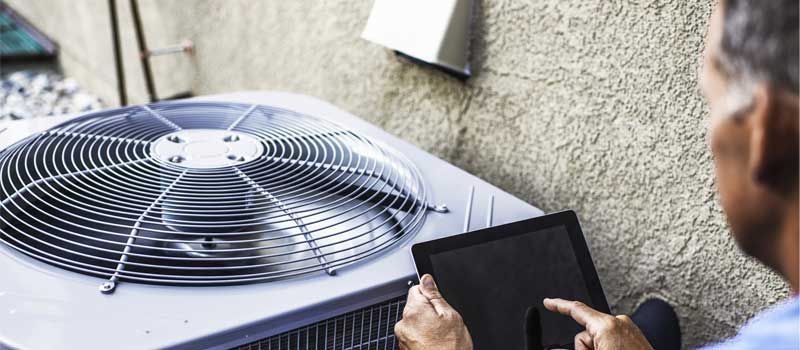 Technician inspecting an outdoor air conditioner unit with a tablet