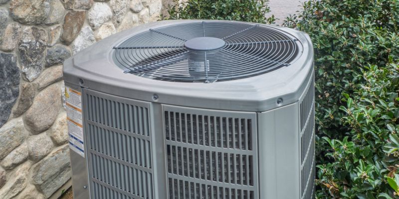 Outdoor air conditioner unit beside a stone wall with a fan on top