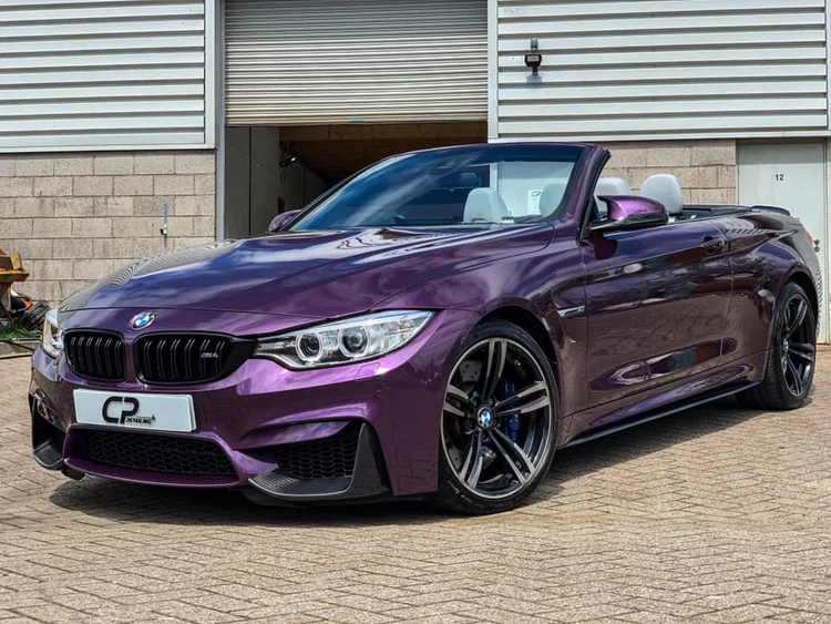 A purple bmw convertible is parked in front of a garage.