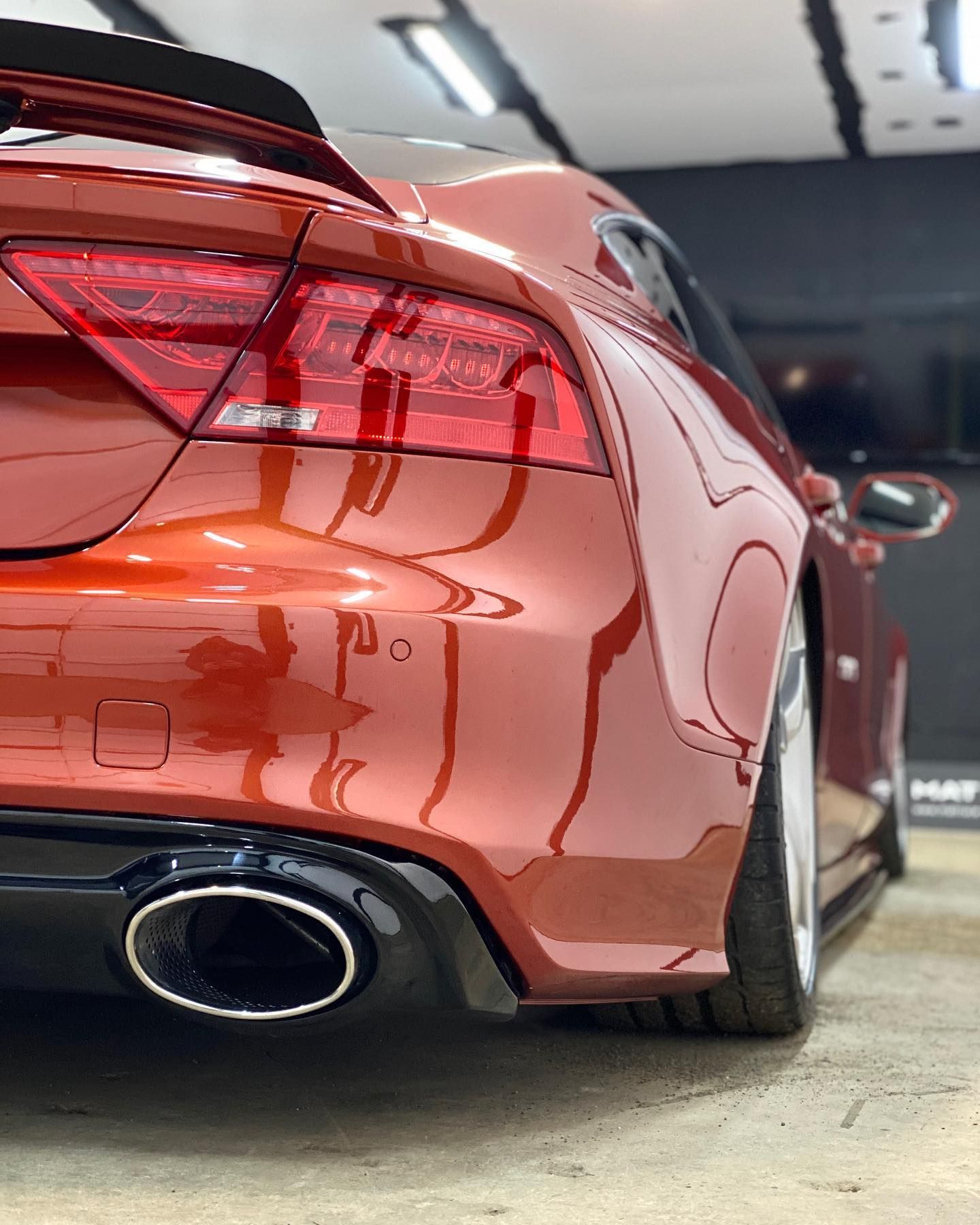 A red car with a black exhaust pipe is parked in a garage.