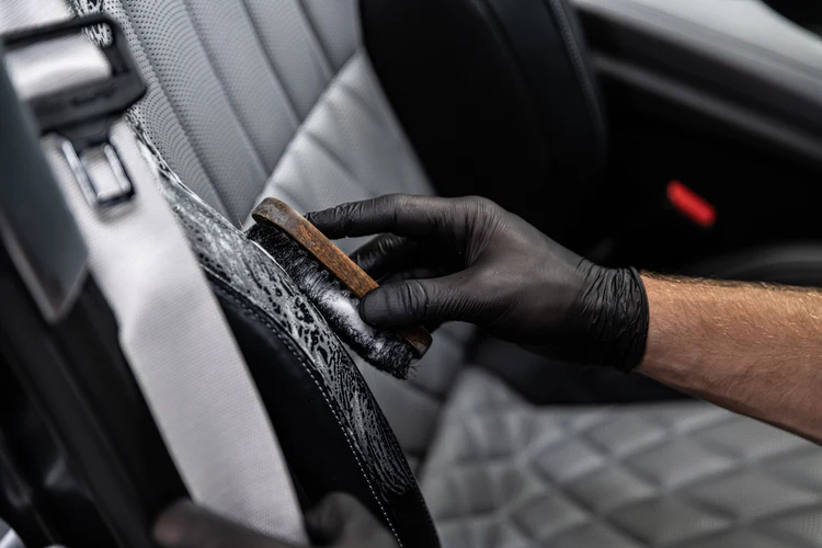 A person is cleaning the seats of a car with a brush.