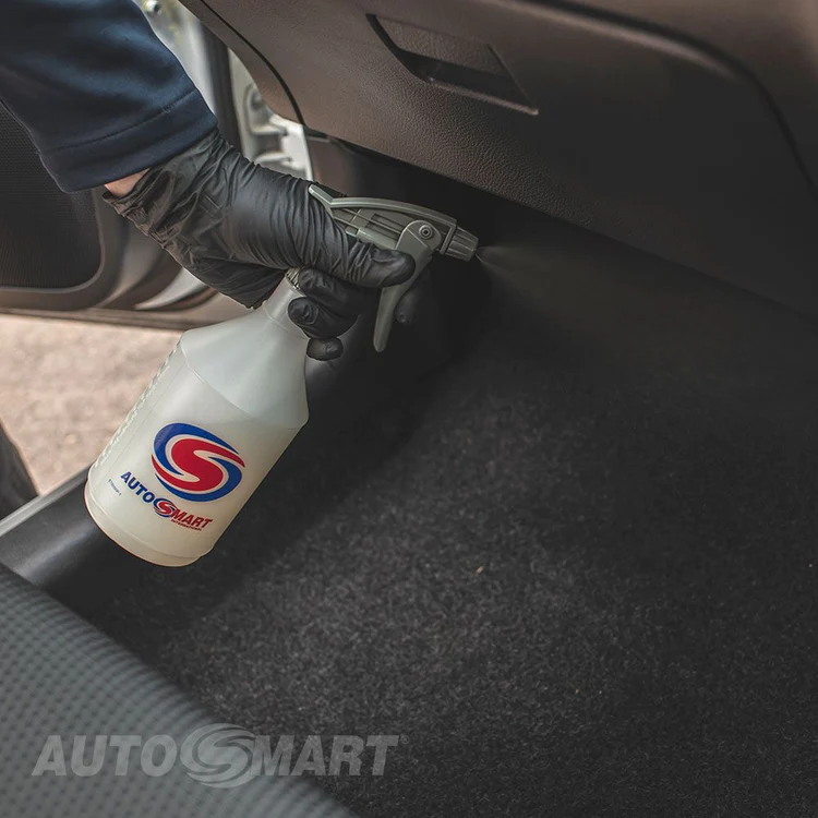 A person is spraying a bottle of autosmart on the floor of a car.