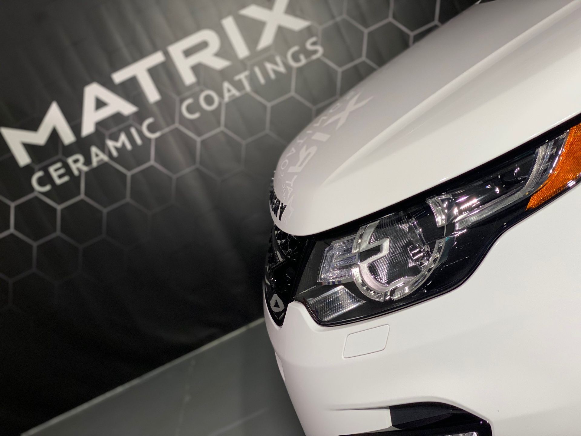 A white car is parked in front of a sign that says matrix ceramic coatings