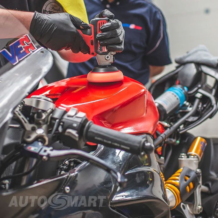 A man is polishing a red motorcycle with gloves on