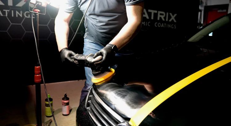 A man is polishing a black car with a polisher.