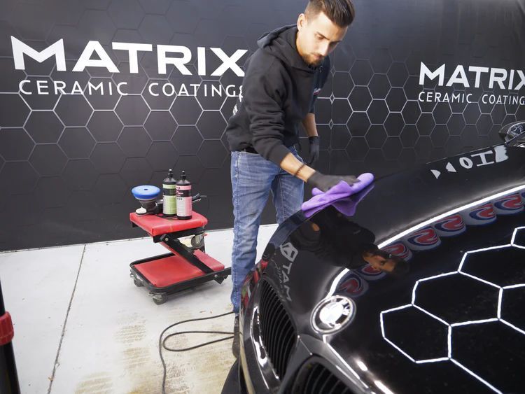 A man is polishing a black car in front of a sign that says matrix ceramic coating