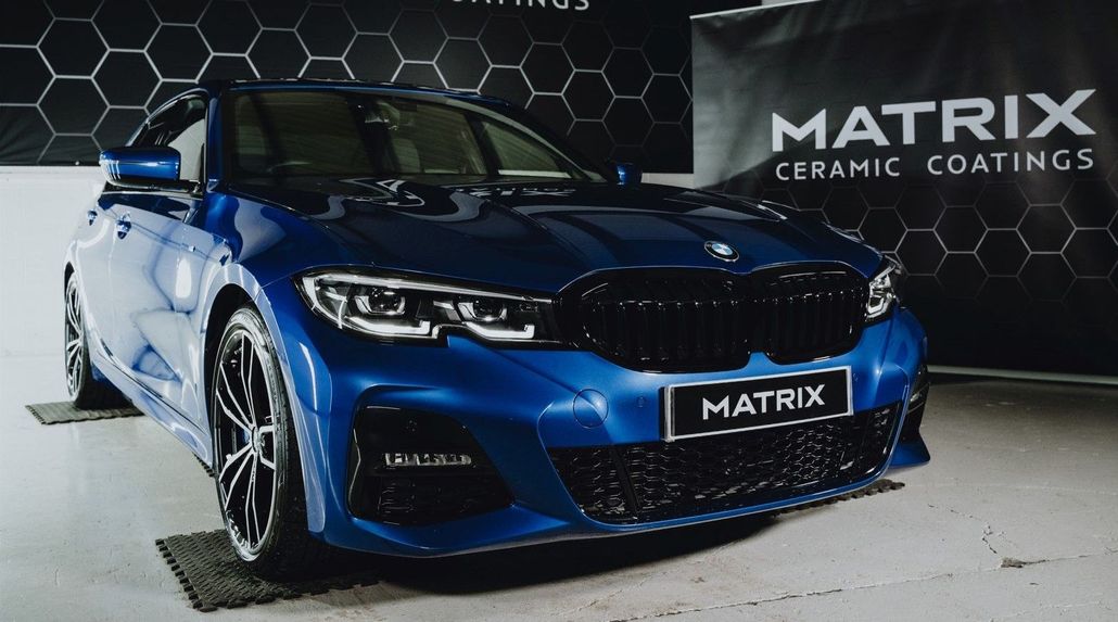 A blue car is parked in front of a sign that says matrix ceramic coatings