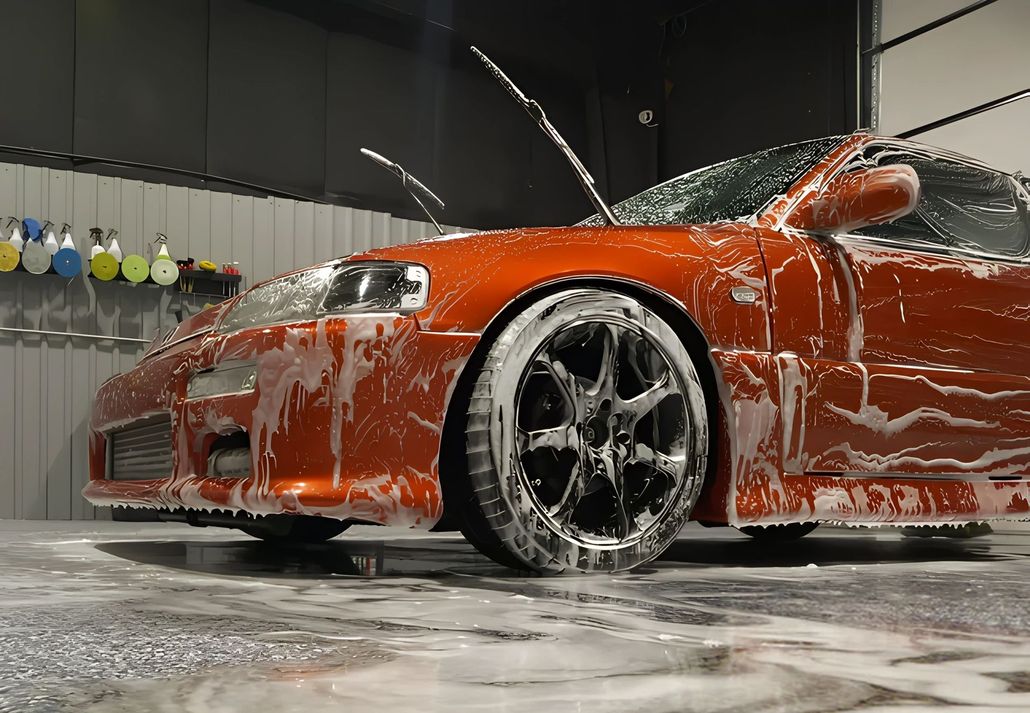 A red sports car is covered in foam in a garage.