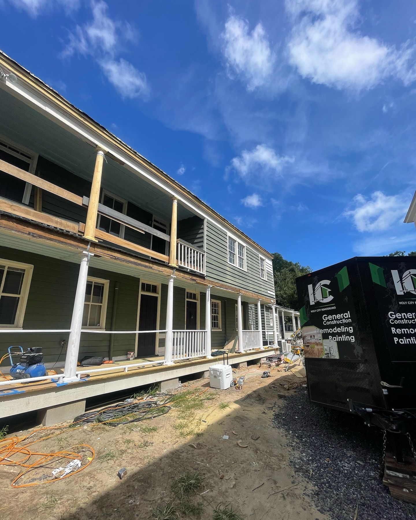 A house under construction with a large porch and a dumpster in front of it.
