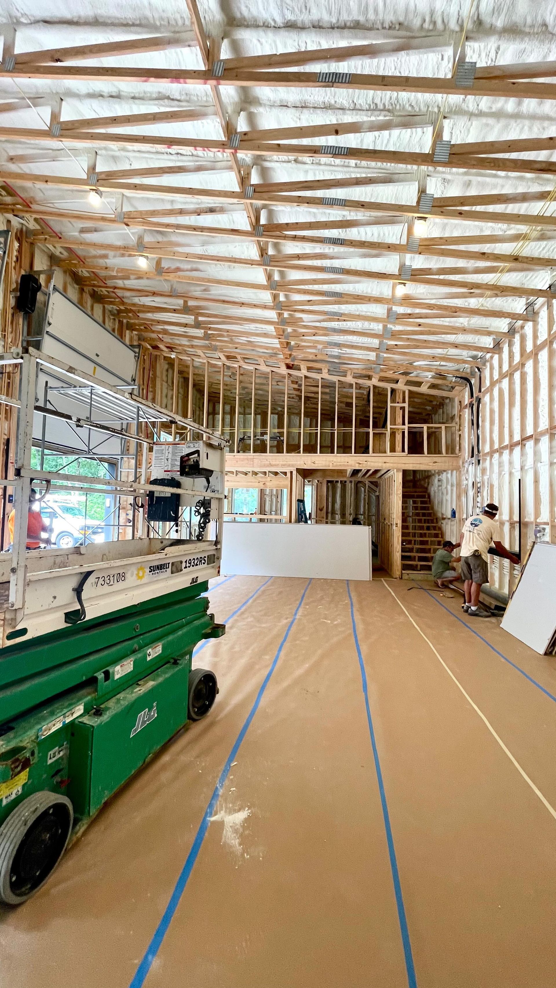 A green scissor lift is sitting inside of a building under construction.