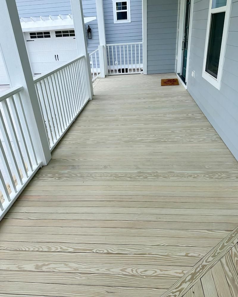 A large wooden porch with a white railing and a door.