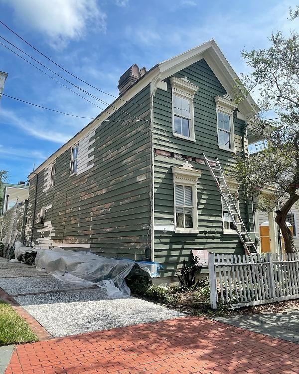 A green house with a ladder on the side of it is being painted.