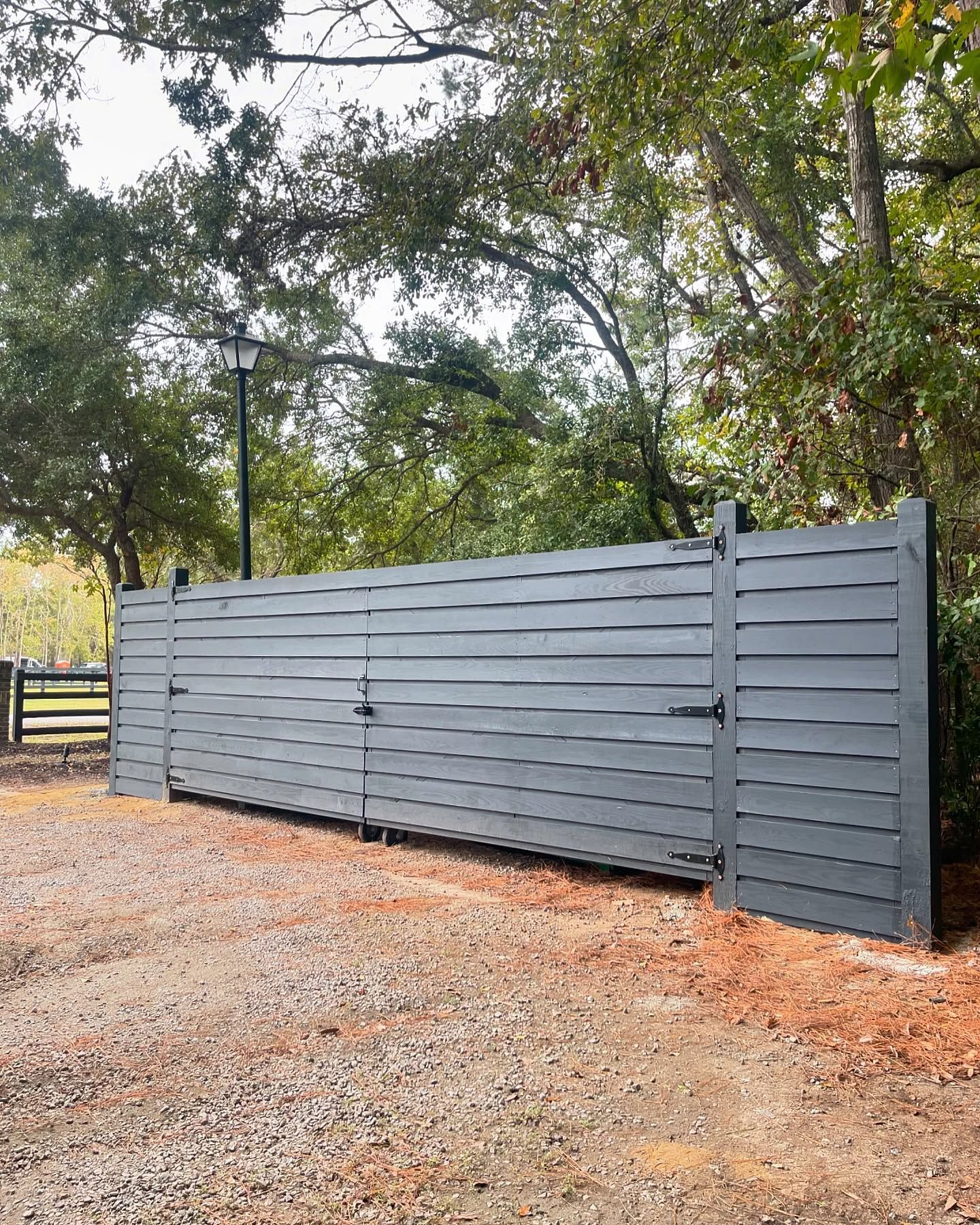 A large wooden fence with a gate in the middle of a gravel driveway.