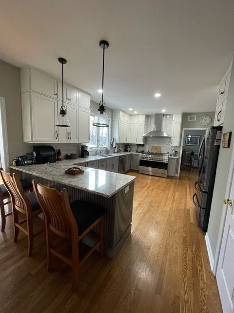 A kitchen with white cabinets , stainless steel appliances , granite counter tops and hardwood floors.