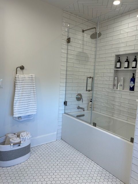 A bathroom with a bathtub , shower , and bottles on the shelves.