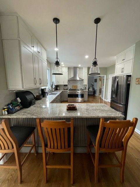 A kitchen with white cabinets , granite counter tops , and wooden chairs.