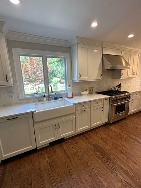 A kitchen with white cabinets , a sink , a stove , and a window.