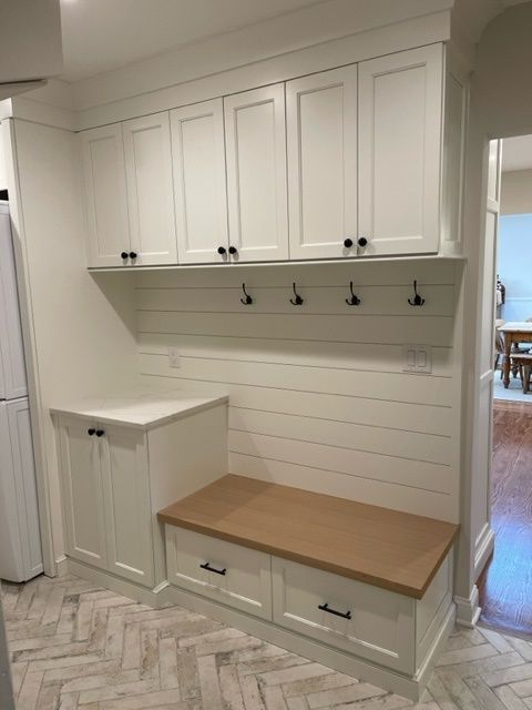 A laundry room with white cabinets and a wooden bench.