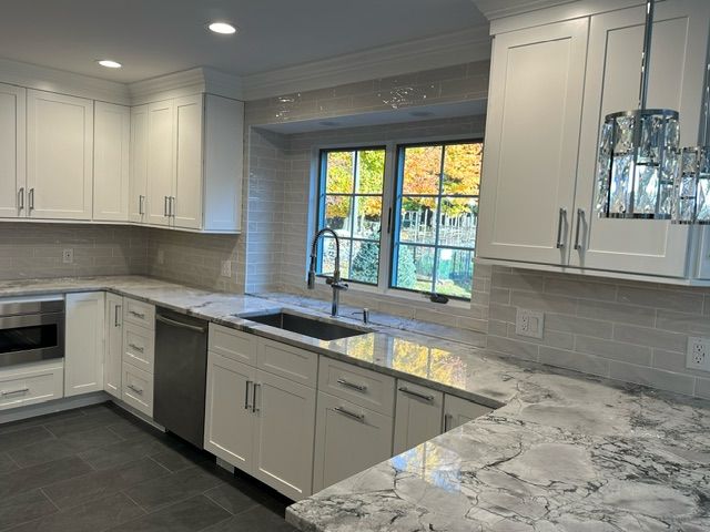 A kitchen with white cabinets , granite counter tops , a sink and a window.