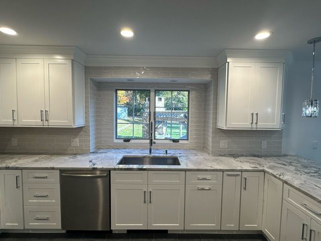 A kitchen with white cabinets , a sink , a dishwasher , and a window.