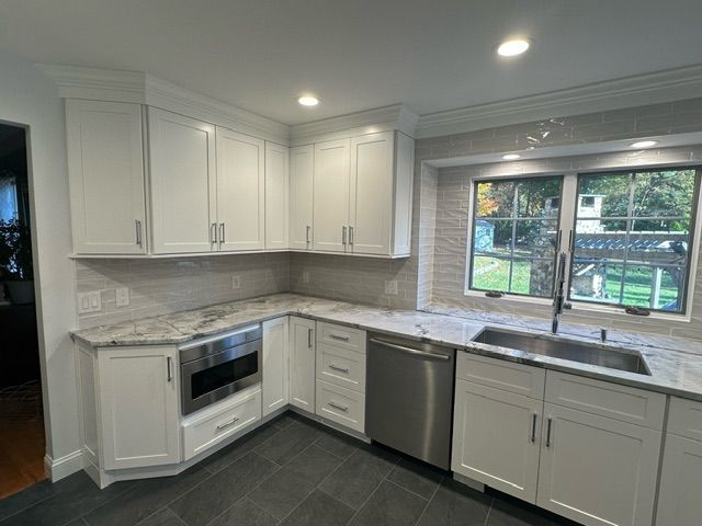 A kitchen with white cabinets , stainless steel appliances , a sink , and a window.