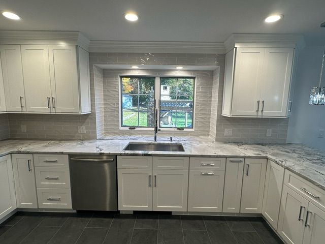 A kitchen with white cabinets , granite counter tops , a sink and a window.