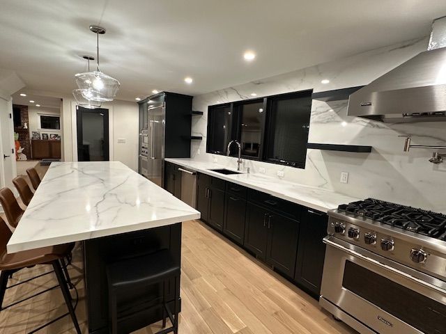 A kitchen with black cabinets , white counter tops , stainless steel appliances and a large island.