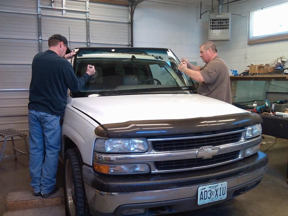 two men are working on a white truck's  windshield