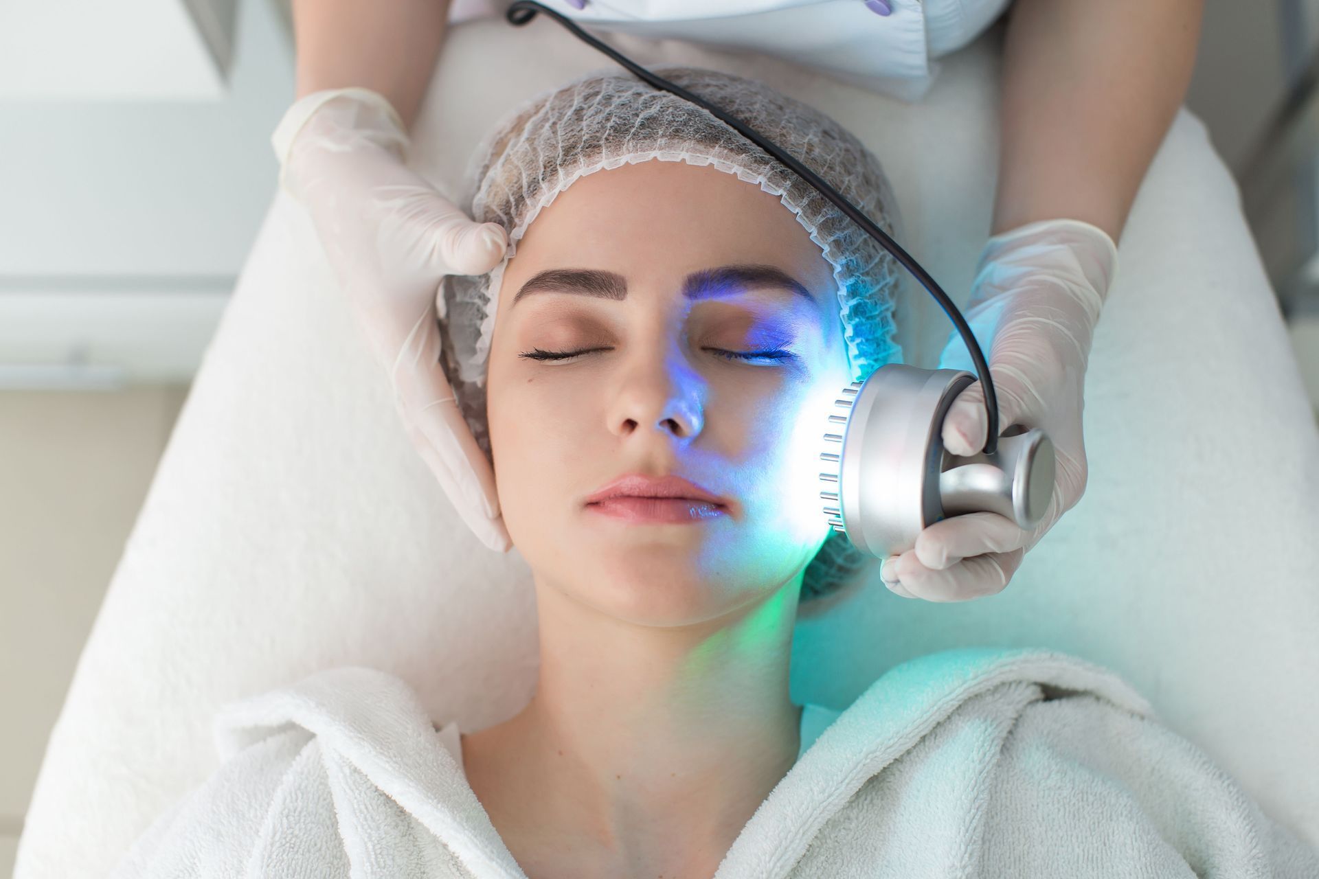 Woman lying on a treatment bed with a facial device and blue light near her cheek